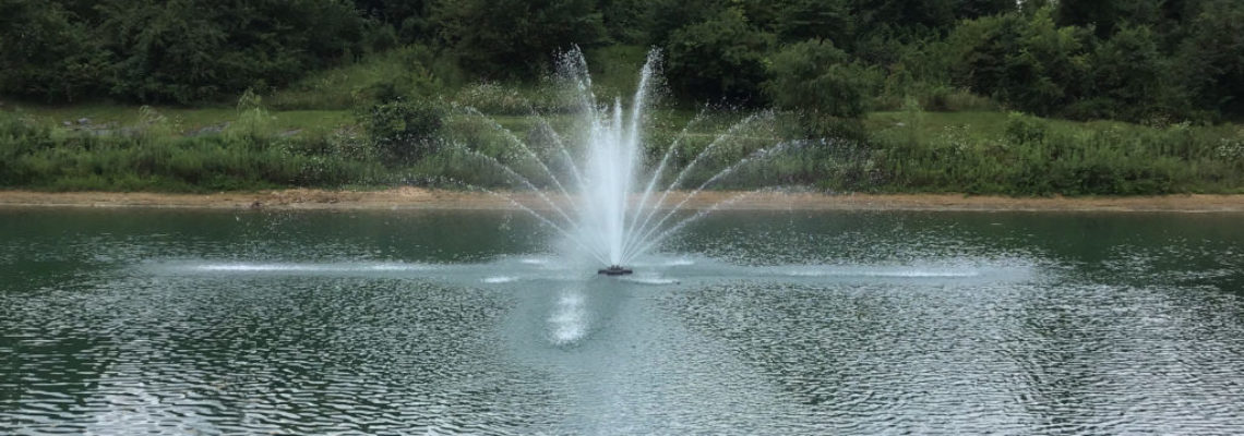 A 5 horsepower fountain sprays a fan of water in the middle of a clean pond